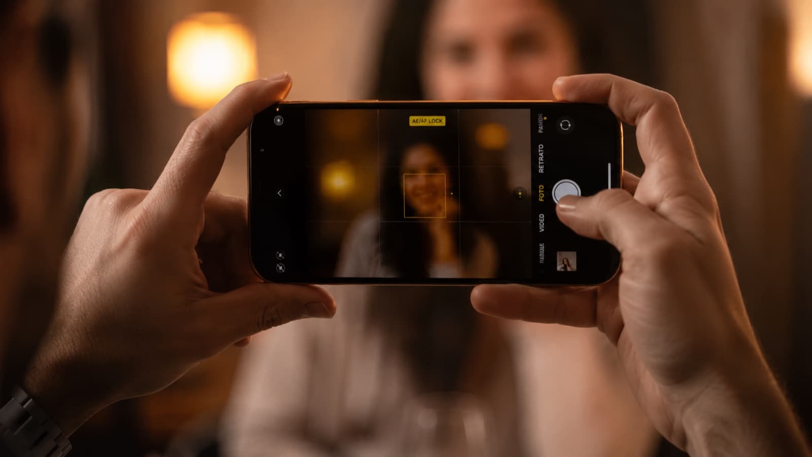 Mãos segurando o celular na horizontal com o indicador AE/AF LOCK e o quadrado de foco travado num rosto