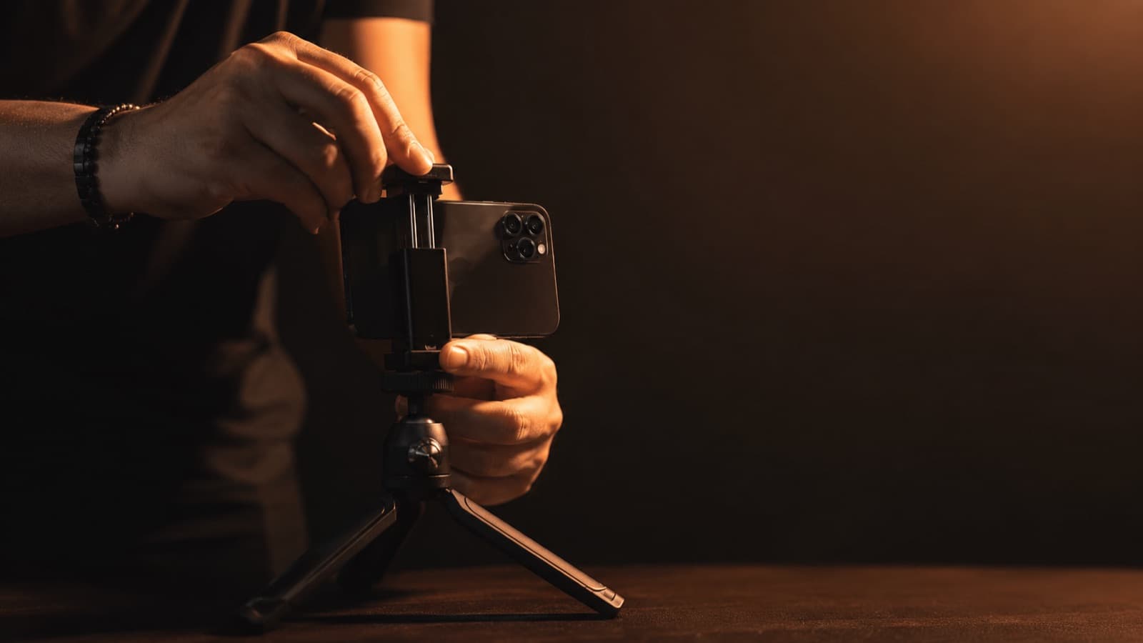Close das mãos encaixando um celular num tripé de mesa, com luz quente ao fundo