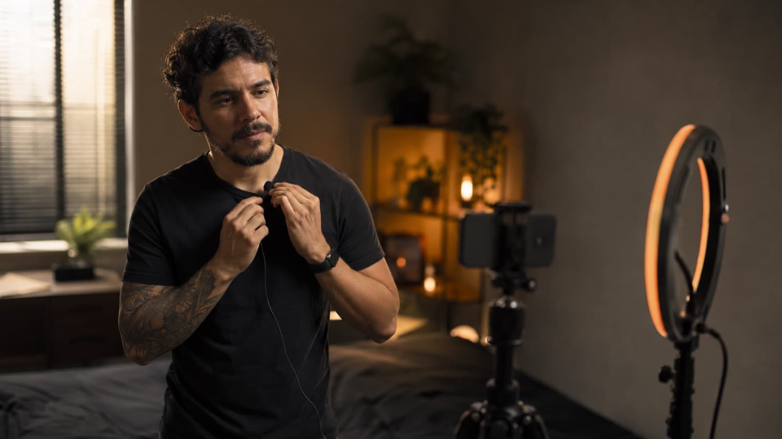 Criador conferindo o microfone lapela num mini-set com ring light, antes de gravar