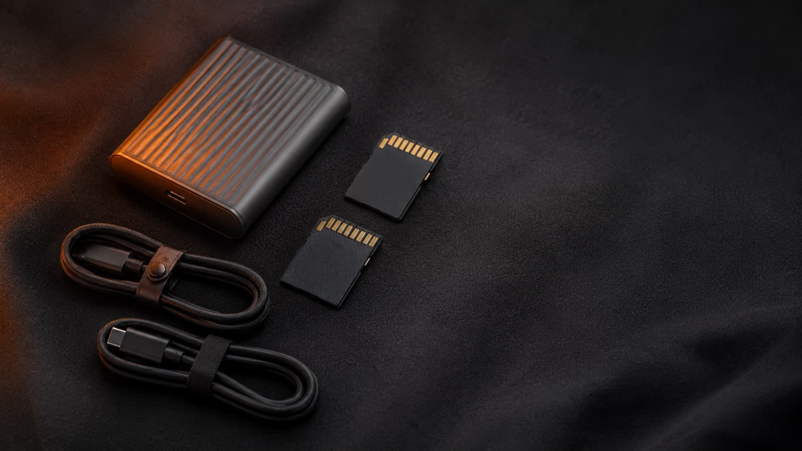 Cartões SD e um SSD portátil com cabos, em flat-lay sobre fundo escuro