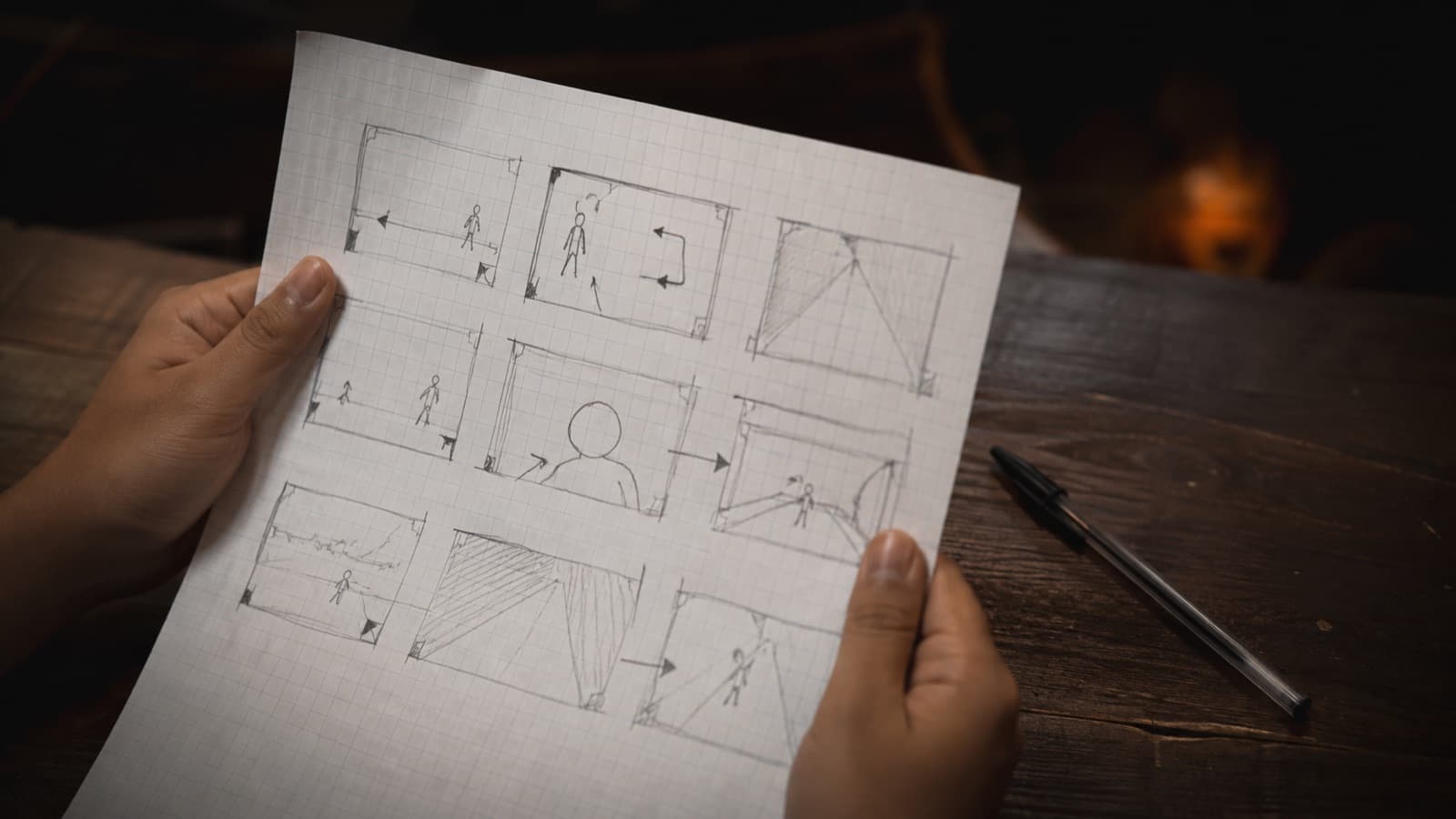 Mãos segurando um storyboard desenhado à mão com bonecos de palito, caixas e setas